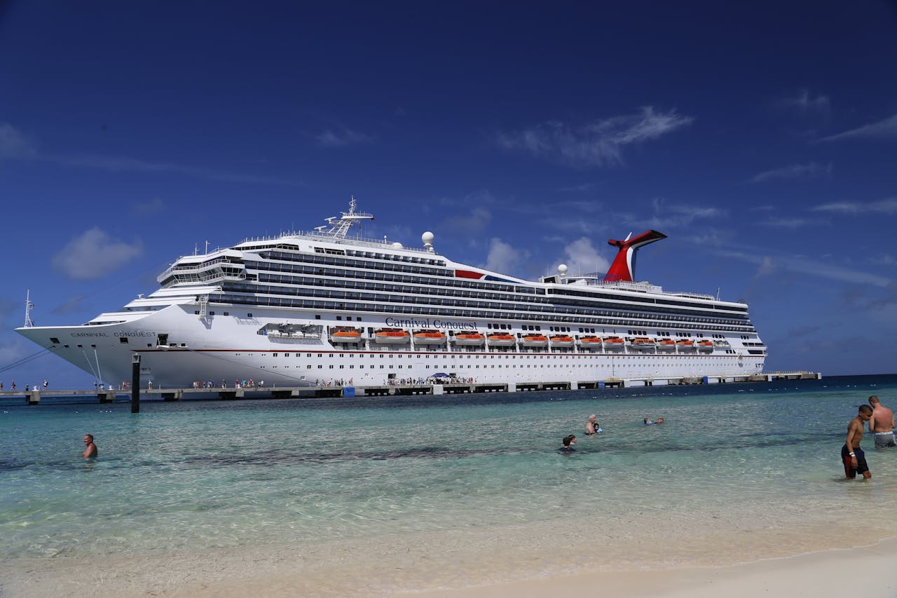 A large white cruise ship anchored by a scenic turquoise water beach in summer.